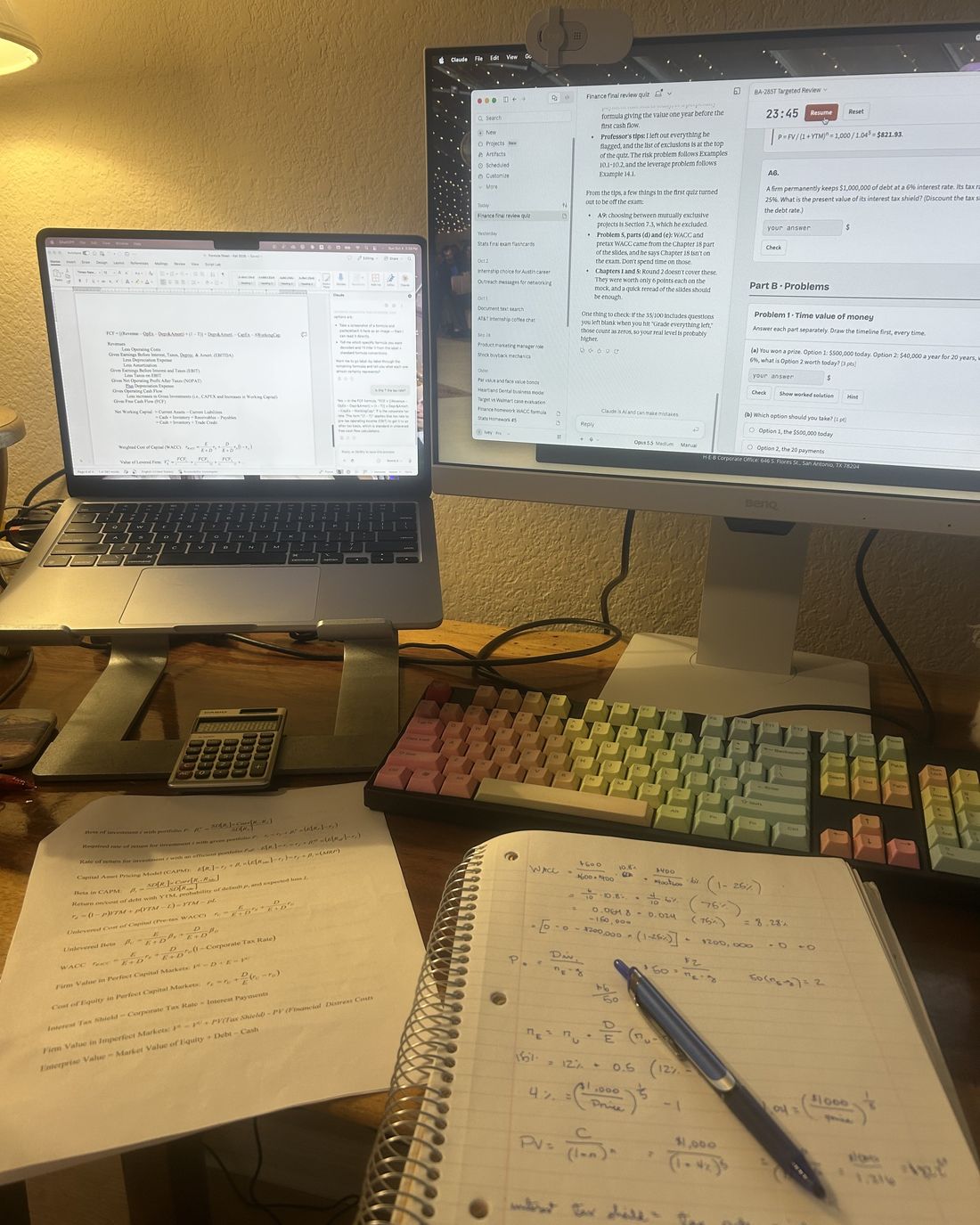 A desk with a laptop, monitor, calculator and handwritten notes